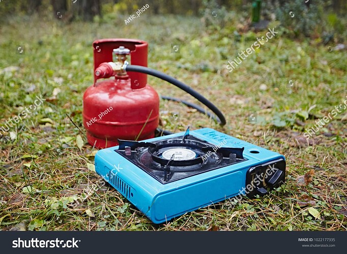 stock-photo-portable-tourist-gas-stove-and-a-balloon-with-a-hose-against-the-background-of-green-grass-and-1022177335
